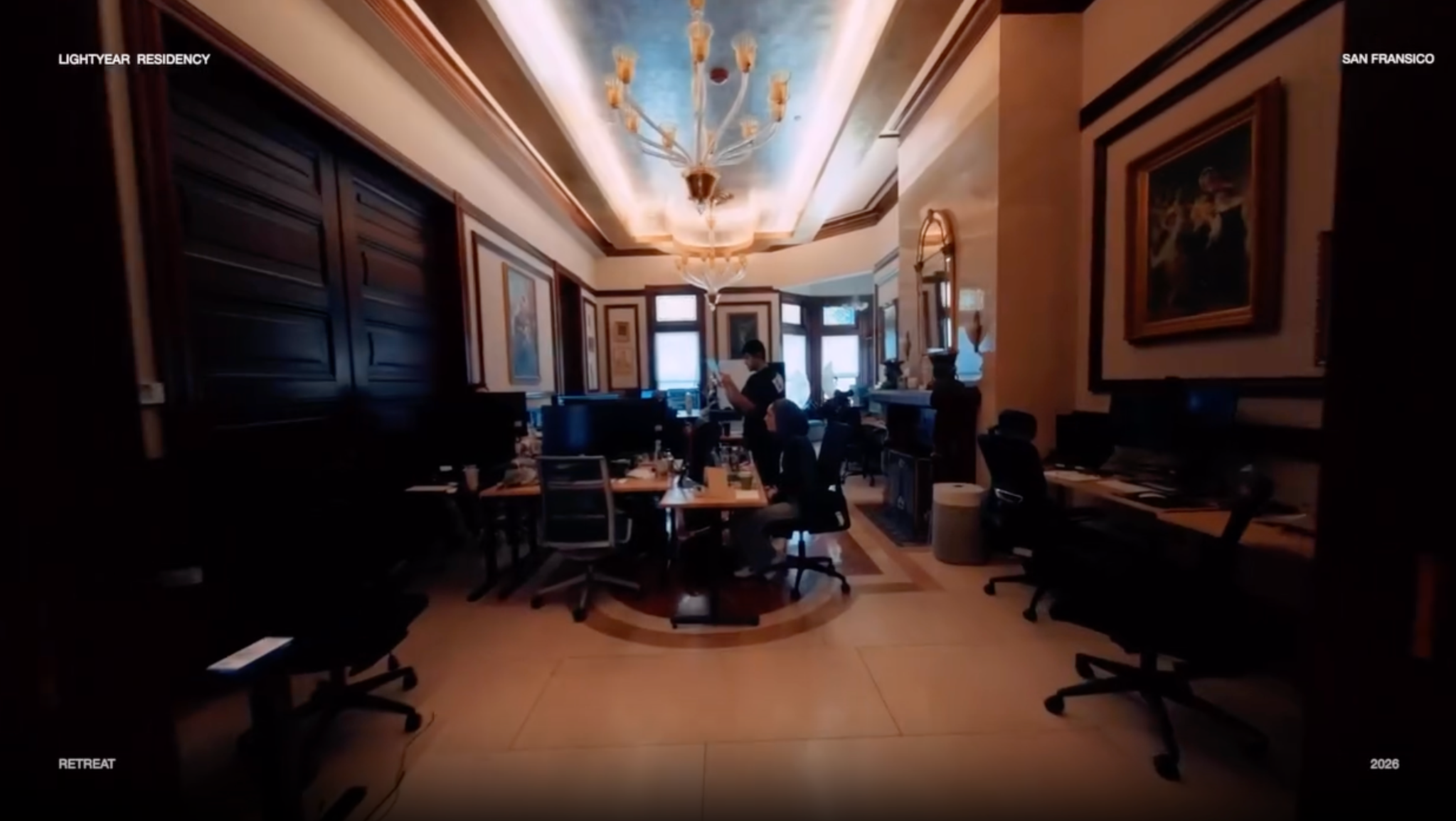 A wide view of the Lightyear Residency workspace, with desks beneath a chandelier.