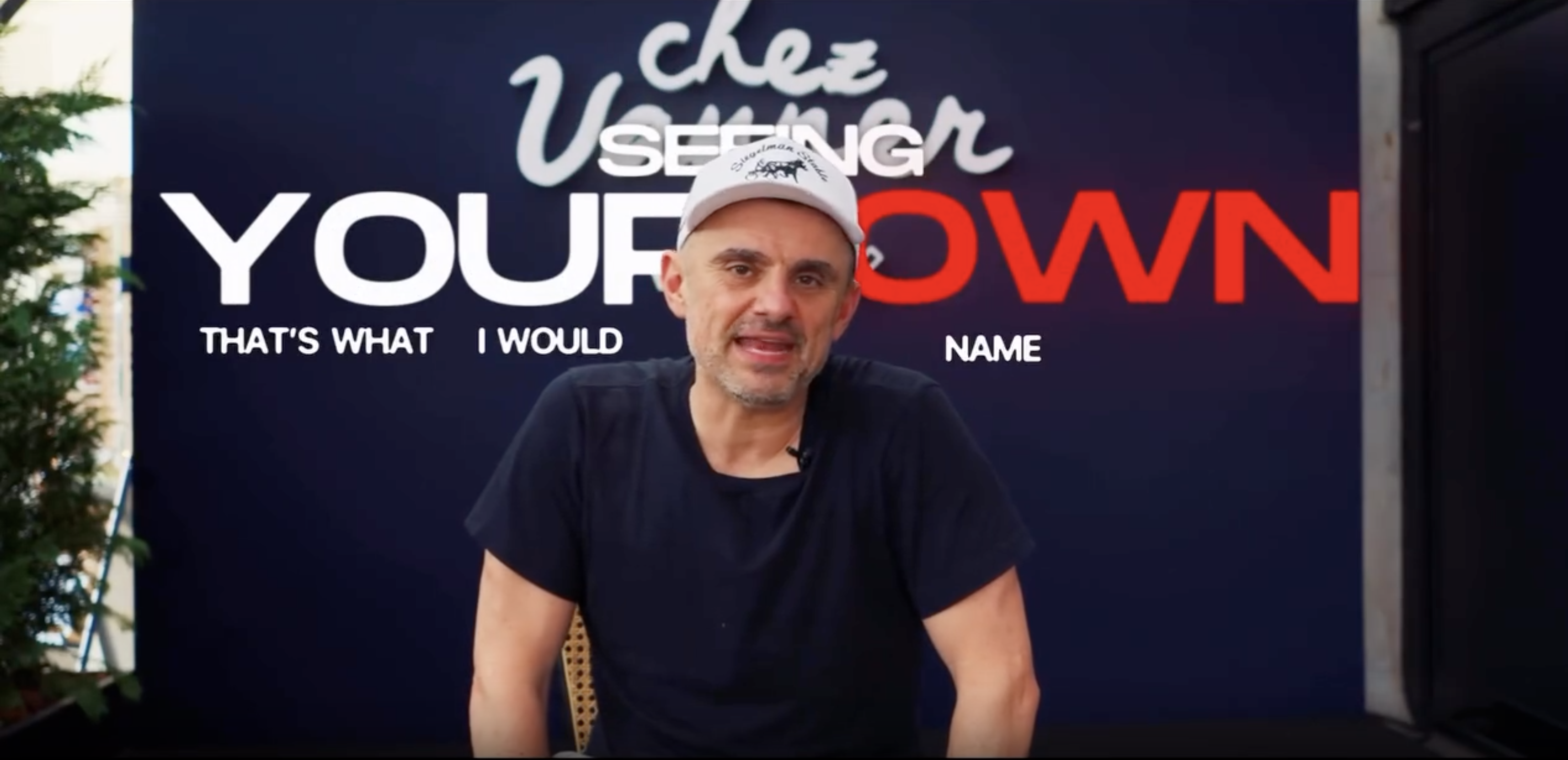 Gary Vaynerchuk in a white cap speaking in front of a Chez Vanner backdrop, with the on-screen words Seeing Your Own Name.